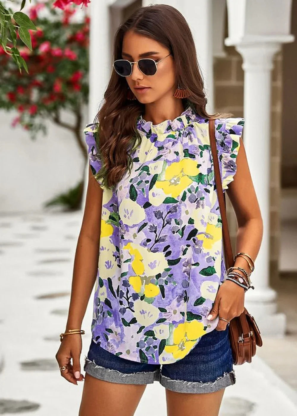 Woman in a yellow, purple, and green floral print ruffled-neck top and denim shorts.