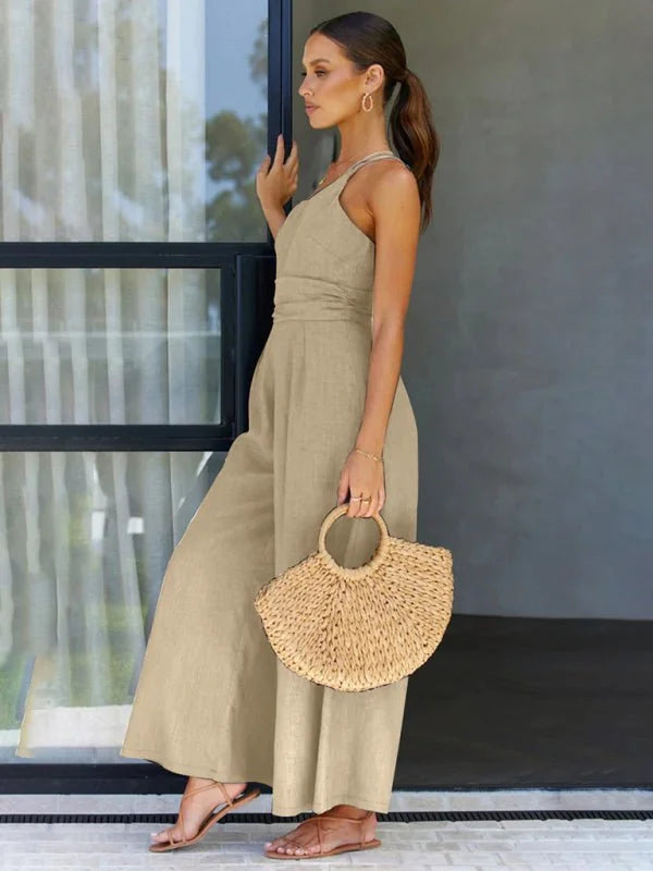 Woman in a tan linen-blend jumpsuit with wide legs and a straw bag.