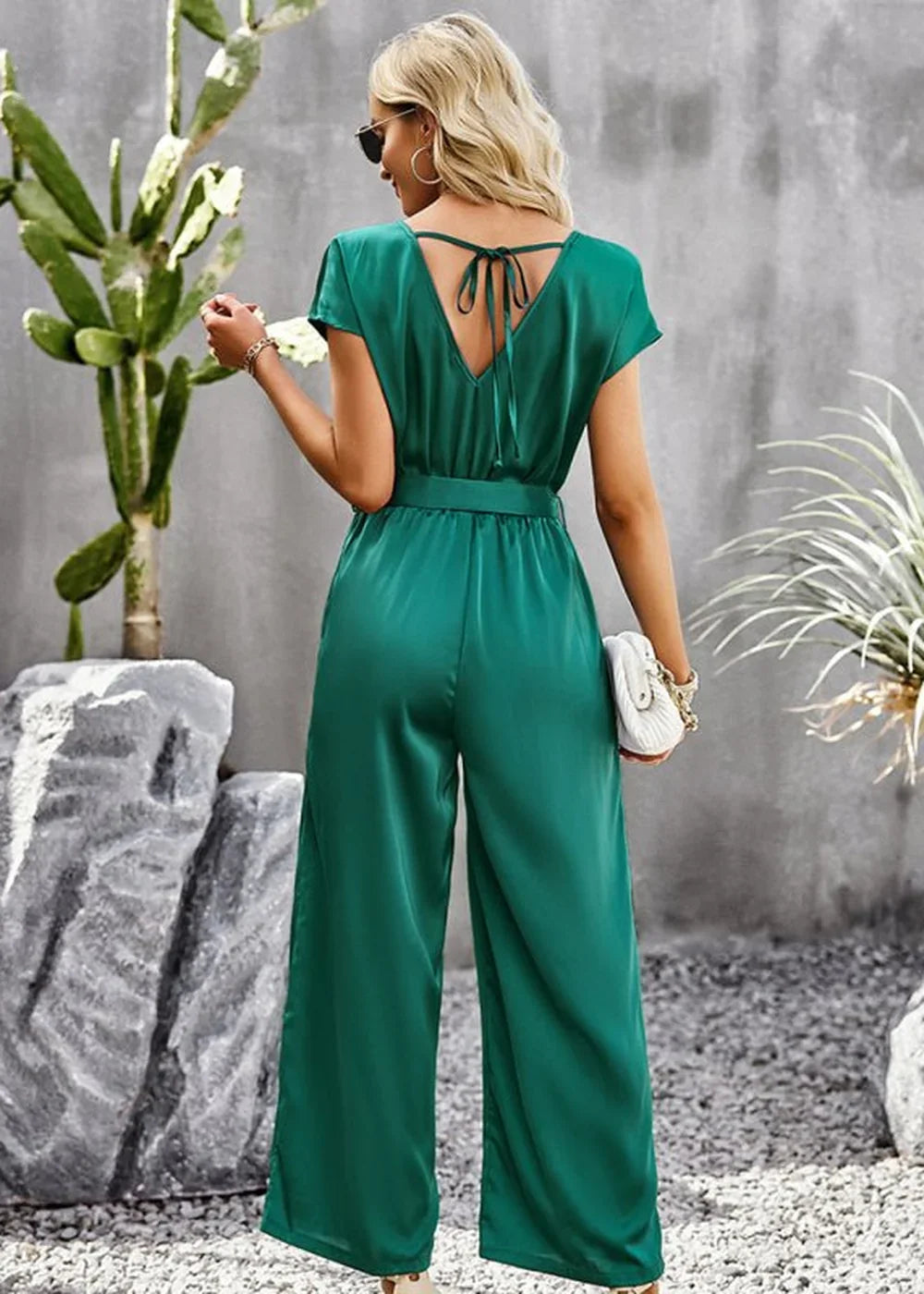 Emerald green satin jumpsuit with a tie-back V-neck and wide legs, shown from the back.