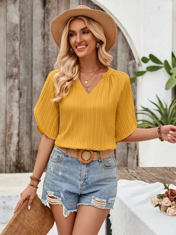 Yellow pleated v-neck top with puff sleeves, paired with distressed denim shorts and a straw belt.