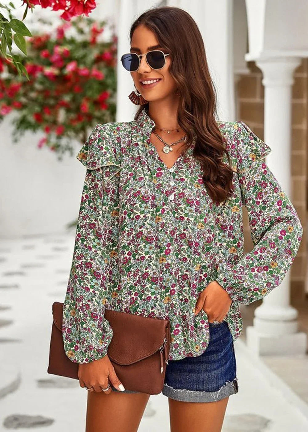 Woman in a green floral print blouse with ruffled sleeves and denim shorts, holding a brown clutch.