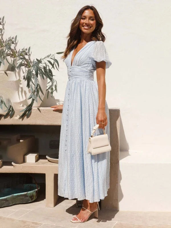Light blue textured midi dress with V-neck and button front, worn by a smiling model holding a cream handbag.
