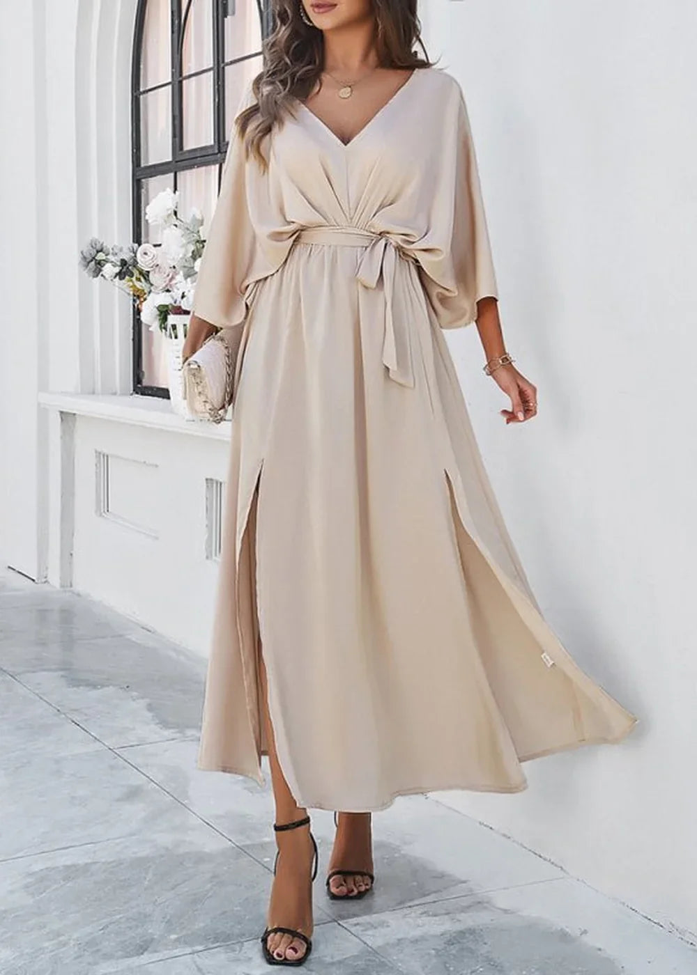 Cream flowy maxi dress with V-neck, belted waist, and high slits on model wearing black heels.