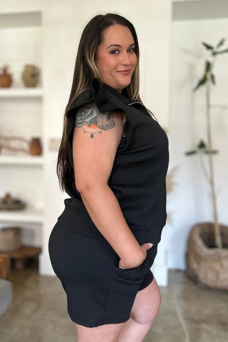 Black textured short suit with ruffle shoulder detail on model with tattoo.