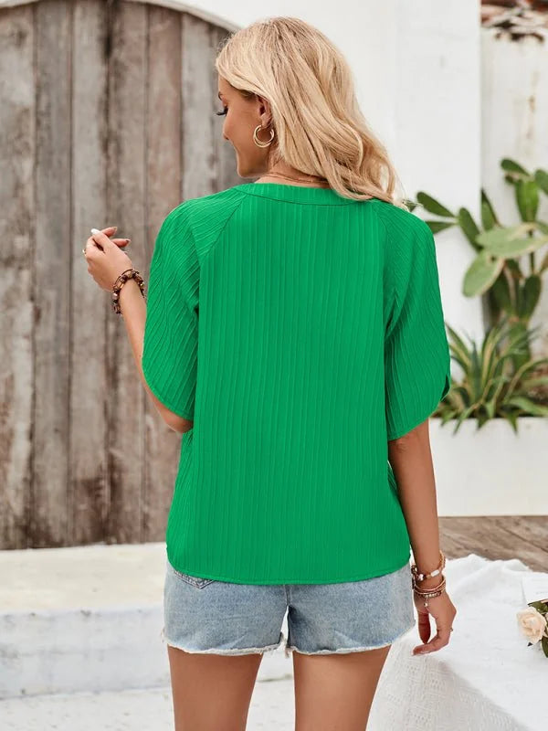 Back view of a woman wearing a bright green, short-sleeved, ribbed top and light wash denim shorts.