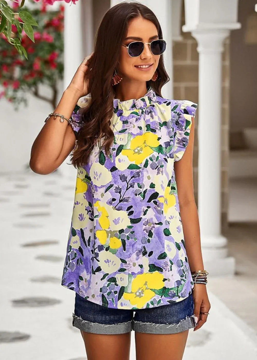 Woman in a vibrant floral print top with ruffled sleeves and denim shorts.