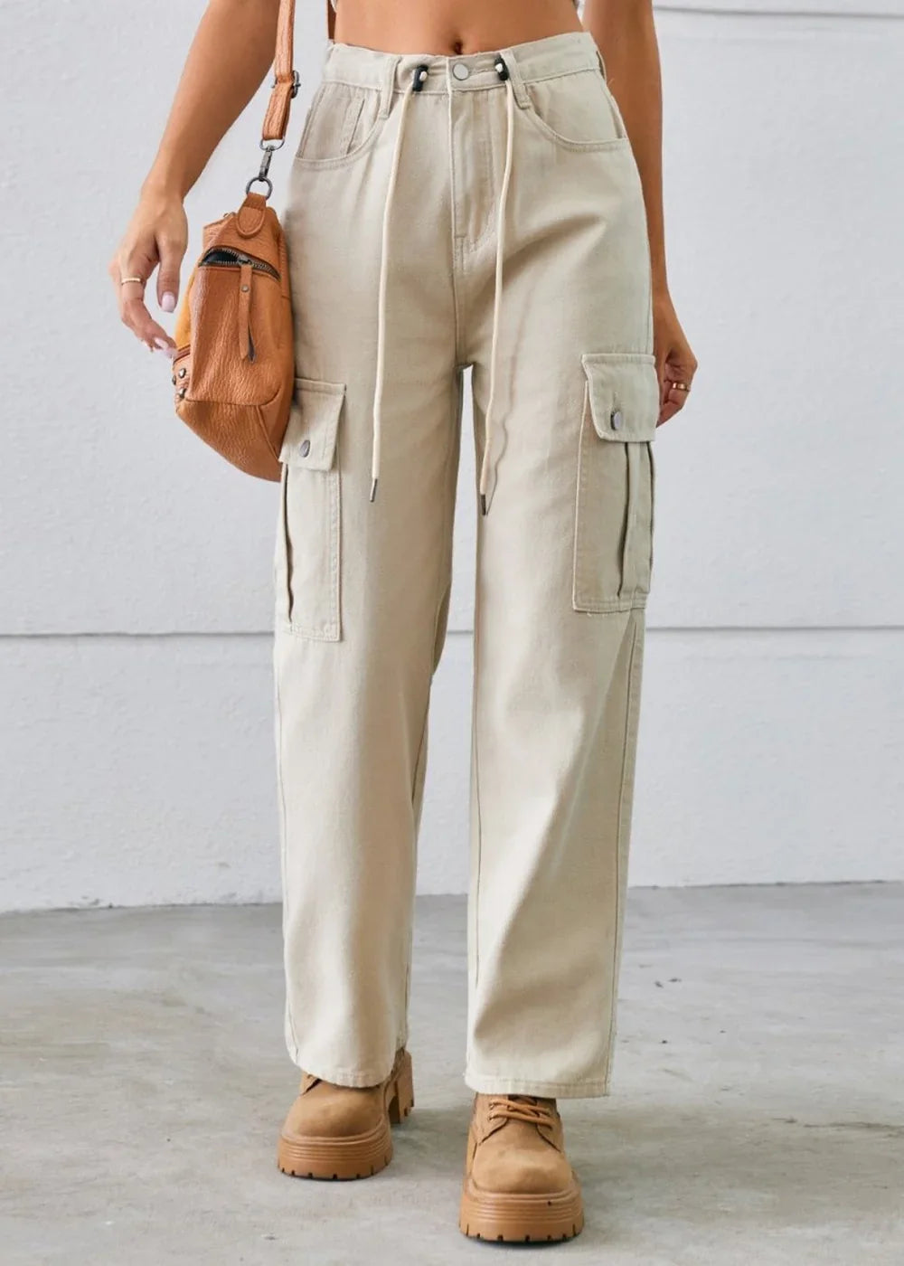 Light beige cargo pants with a drawstring waist and button-flap pockets, worn with brown lace-up boots.