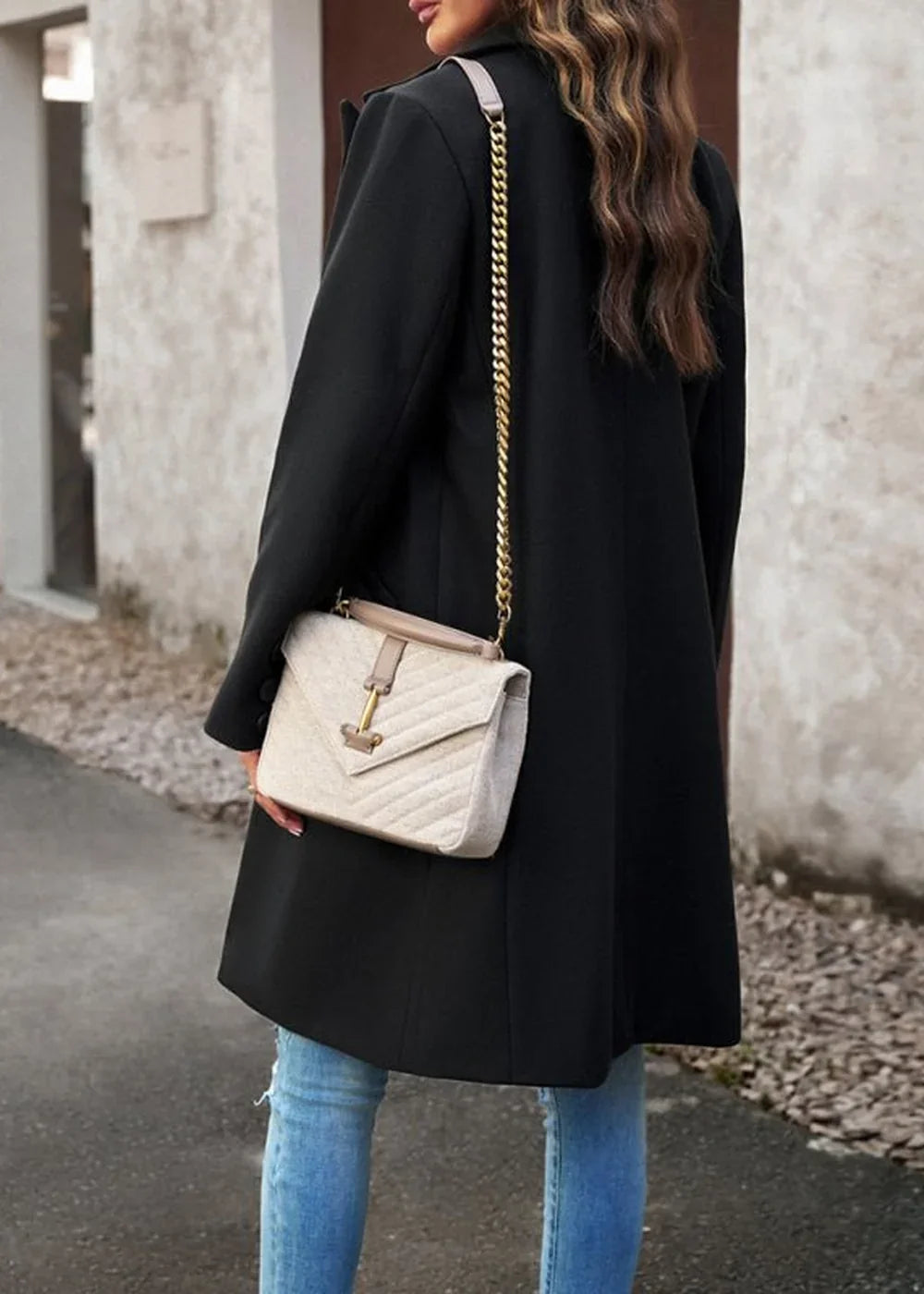 Woman in a black polyester coat and distressed blue jeans, carrying a cream quilted crossbody bag with a gold chain.