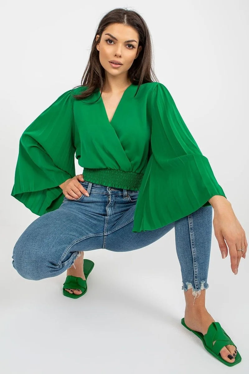 Emerald green wrap top with pleated bell sleeves and distressed blue jeans on a model.