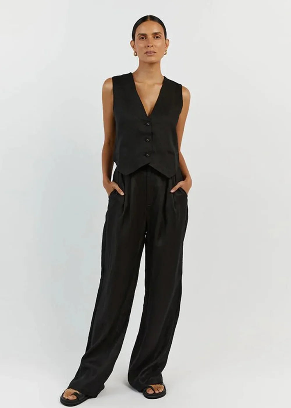 Woman in a black linen vest and wide-leg pants, standing with hands in pockets.