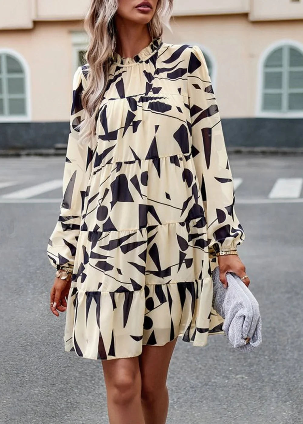 Cream and black abstract print tiered mini dress with long sleeves, on a model.
