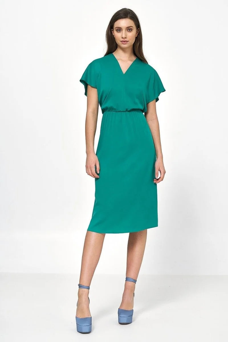 Emerald green midi dress with V-neck and elastic waist, worn by a model with blue platform heels.