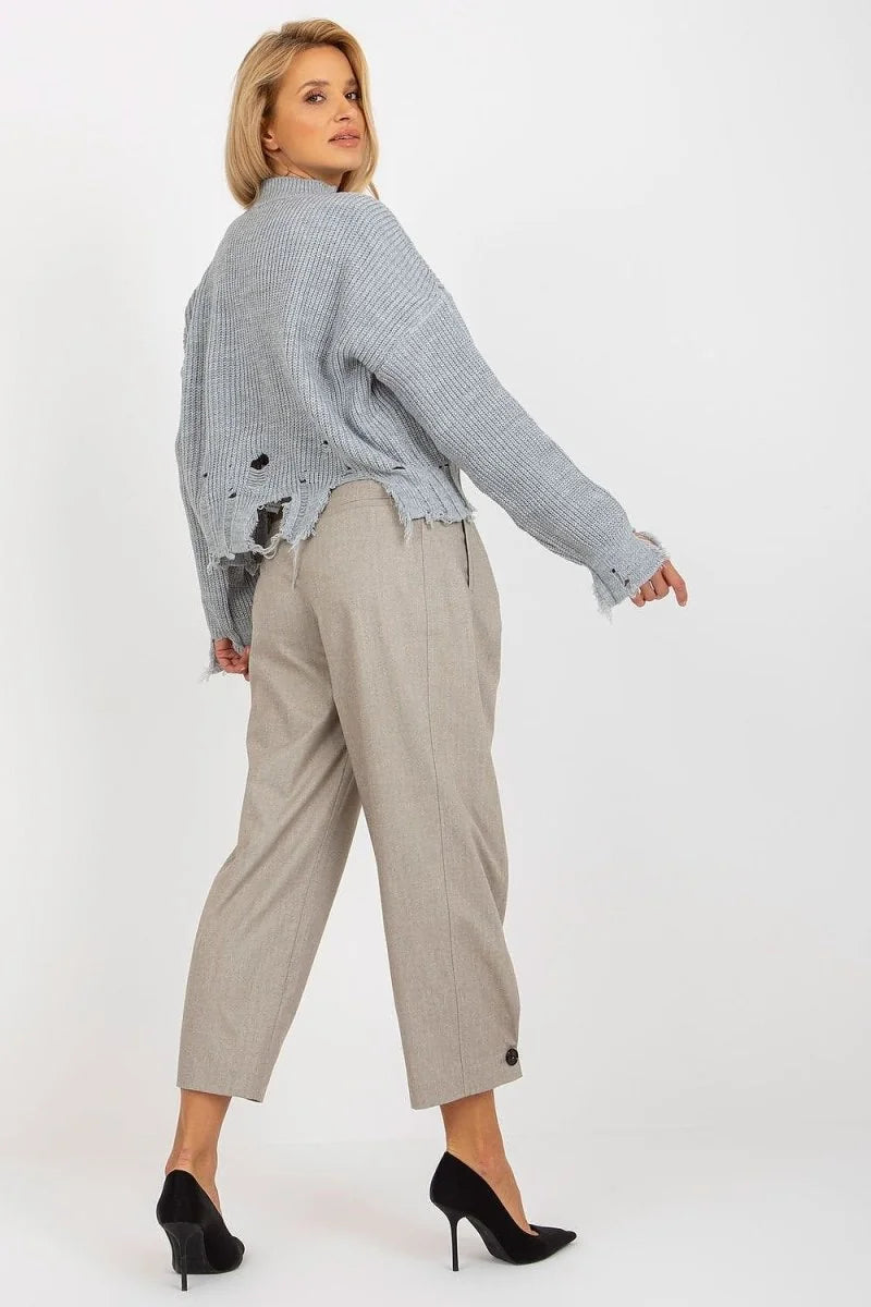 Light blue distressed knit sweater with frayed hem, worn by a woman in beige pants and black heels.