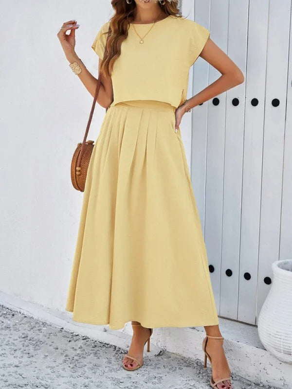 Pale yellow two-piece set with a cropped top and pleated midi skirt, worn by a model.