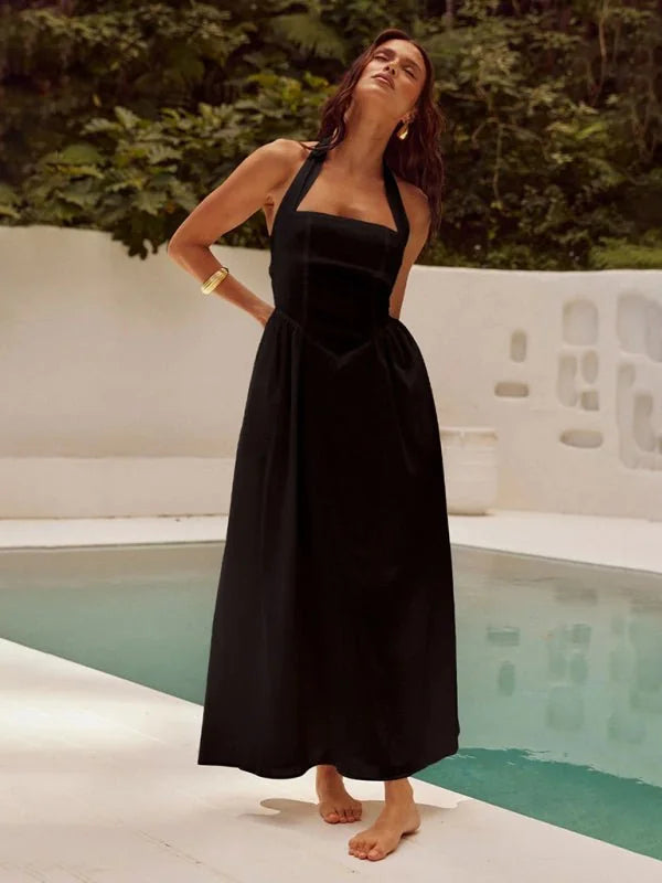 Black halter neck maxi dress with a square neckline and empire waist, worn by a model by a pool.