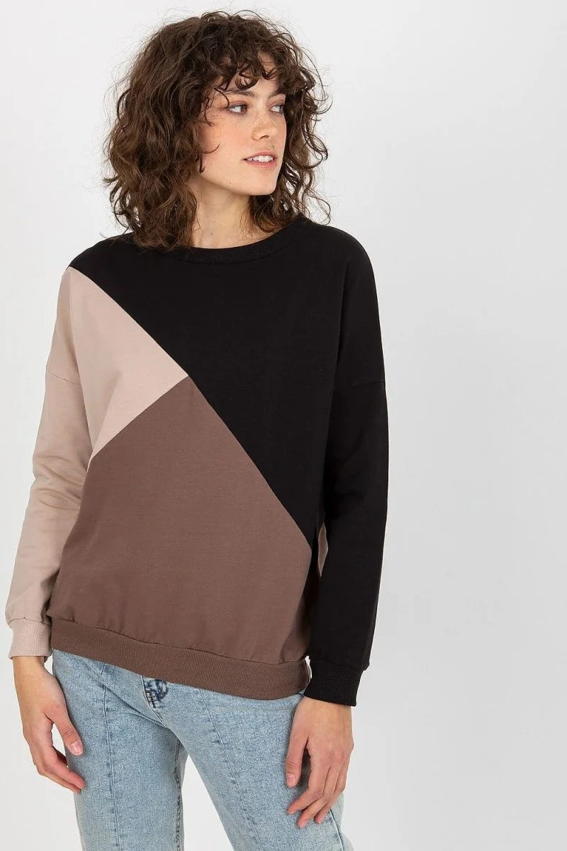 Model in a colorblock sweatshirt with black, beige, and brown panels and light wash jeans.