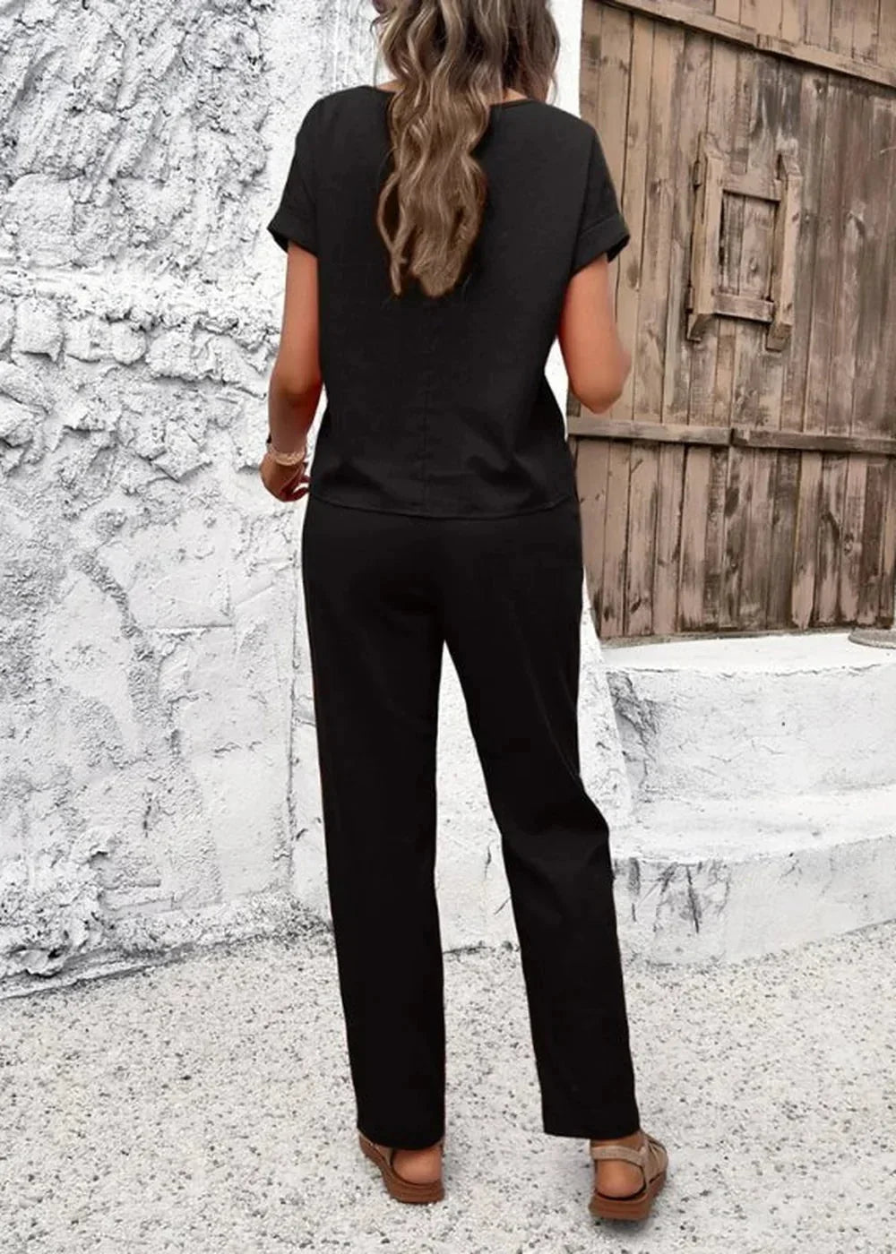 Back view of a woman wearing a black linen-blend pant suit with short sleeves and wide-leg pants.