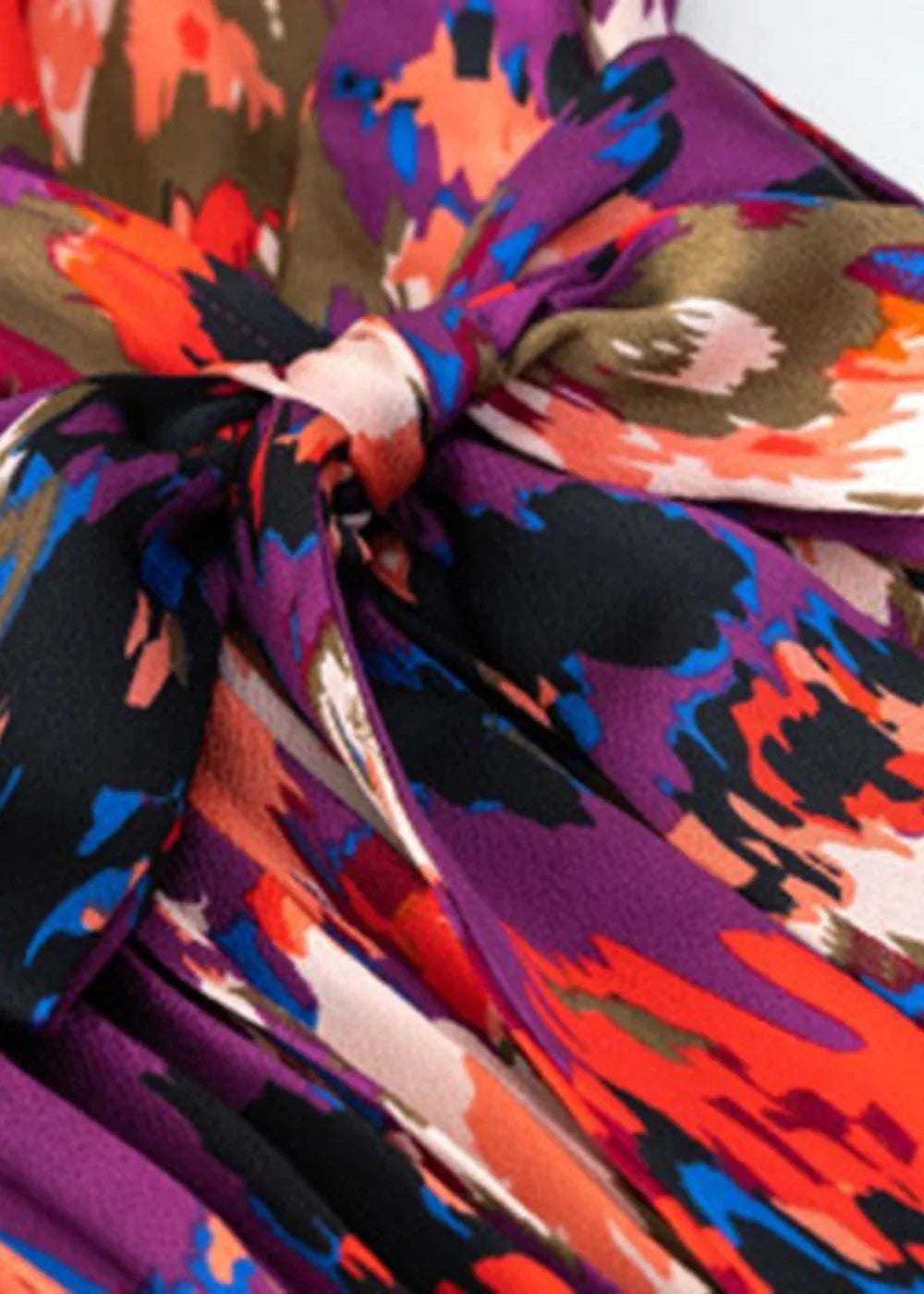 Close-up of a vibrant, abstract floral print dress in purple, orange, and black with a knot detail.