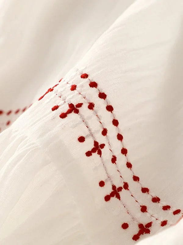Close-up of white fabric with delicate red embroidered dots and cross stitch pattern.