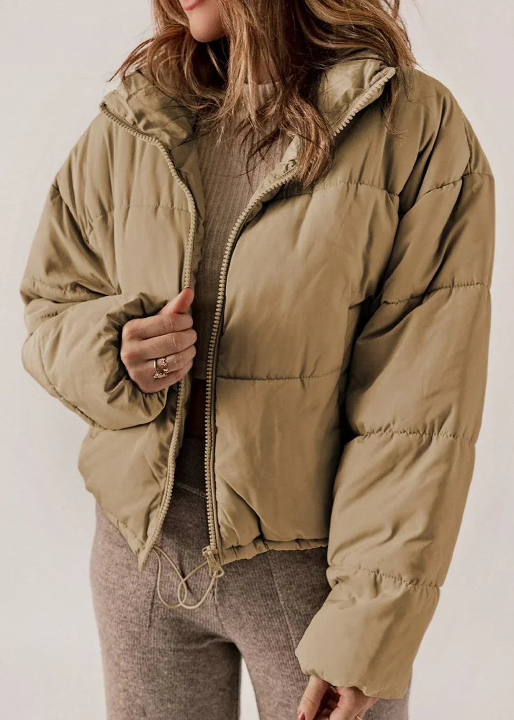Tan puffer jacket with full zip closure and textured knit pants on a model.