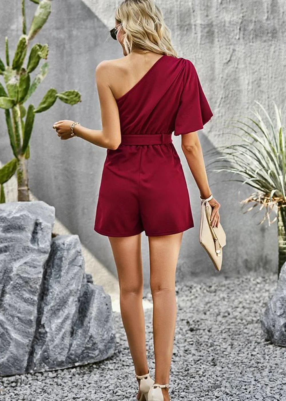 Burgundy one-shoulder romper with belted waist and short sleeves, shown from the back.