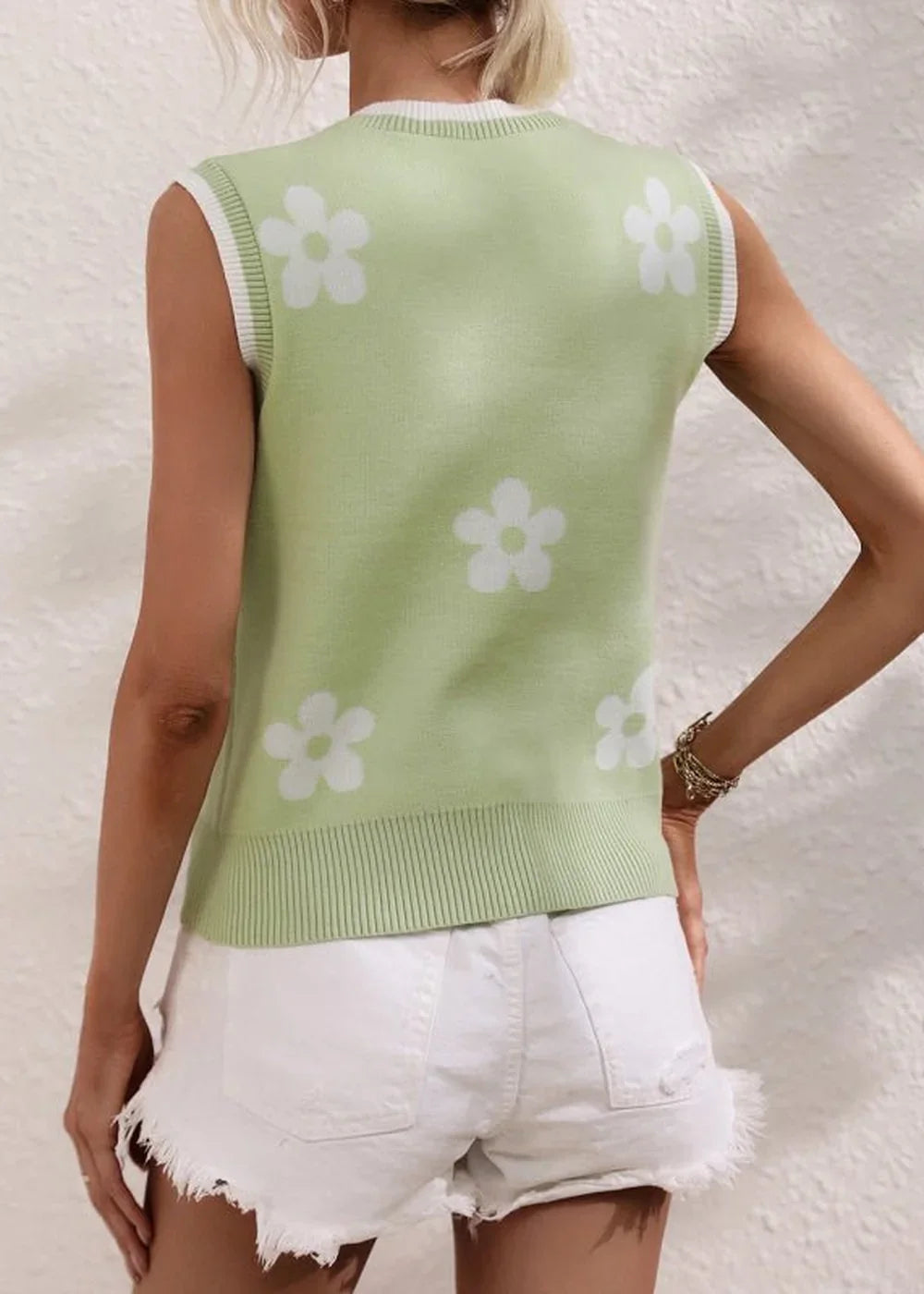 Light green knit vest with white floral pattern and ribbed trim, worn with white denim shorts.