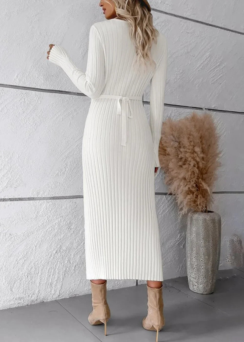 Back view of a white ribbed knit sweater dress with a tie waist and beige ankle boots.