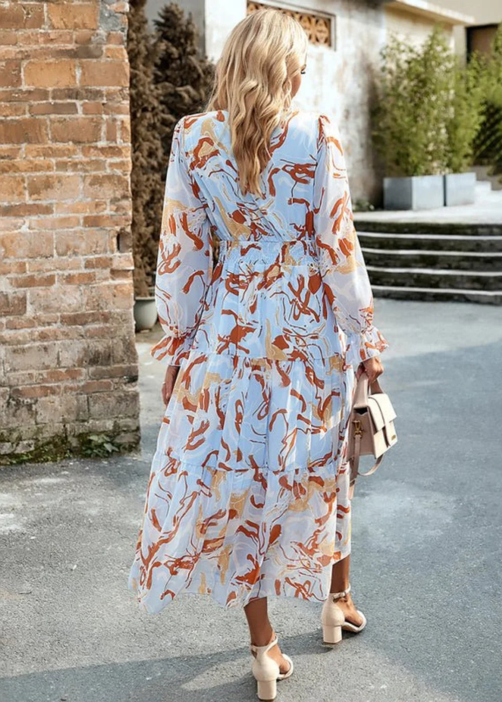 Light blue tiered maxi dress with abstract rust and orange print, long sleeves, cinched waist, on model.