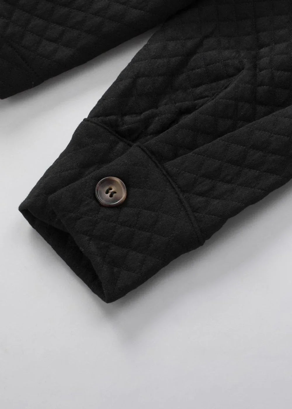 Close-up of a black quilted jacket sleeve with a brown button closure.