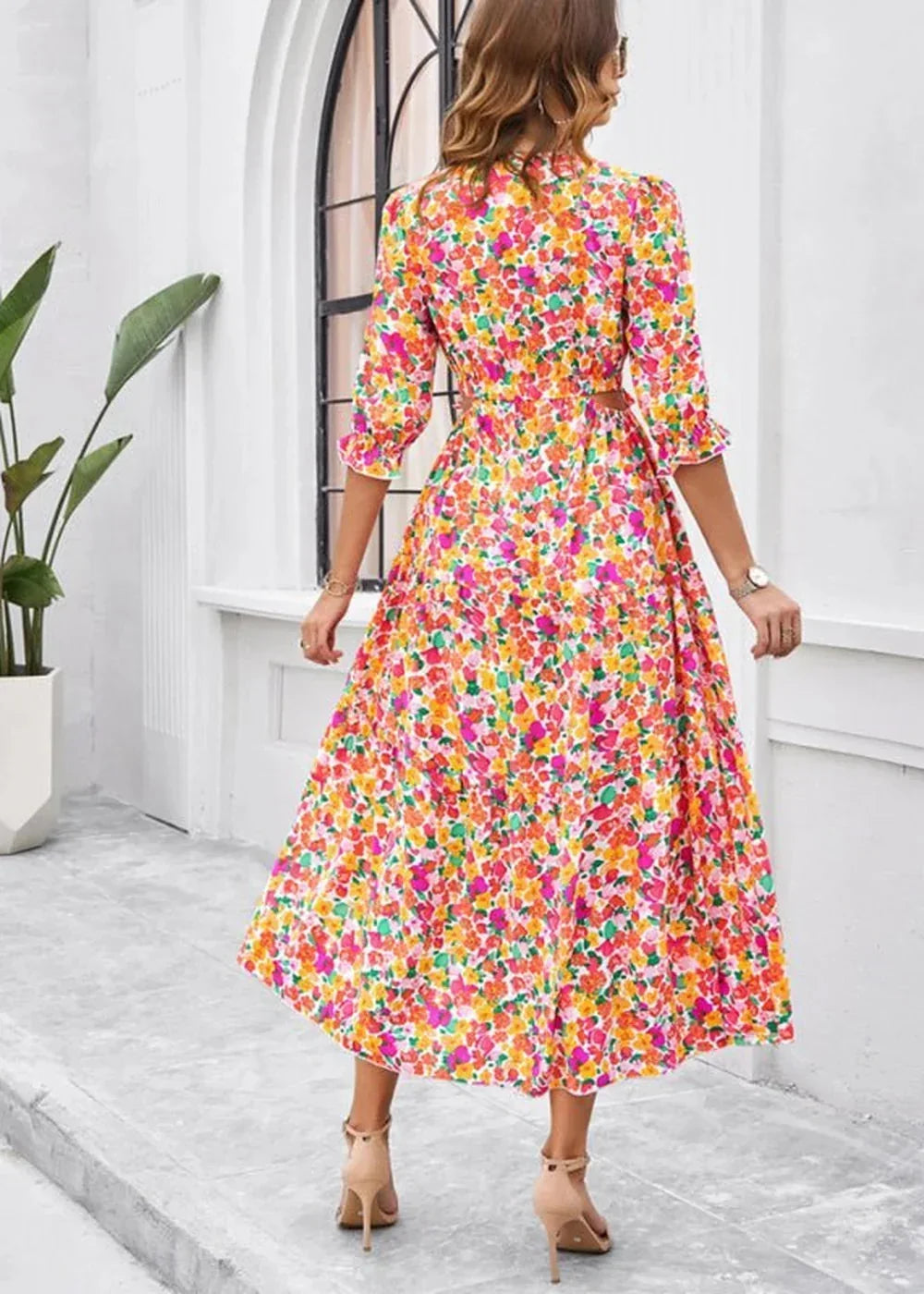 Woman in a vibrant floral print midi dress with ruffled sleeves and high heels, seen from the back.