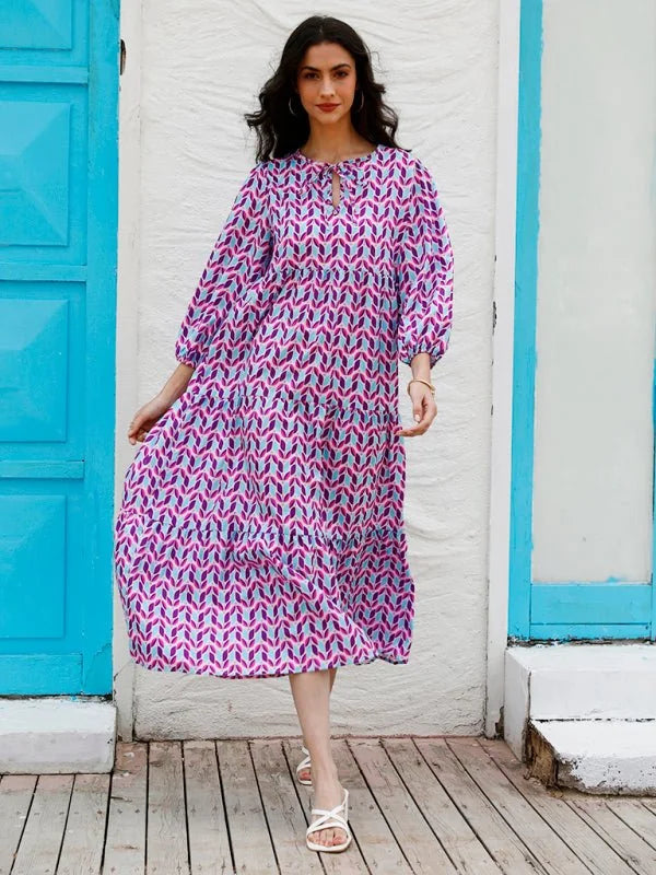 Tiered midi dress with geometric pattern in pink, purple, and blue, on a woman with white sandals.