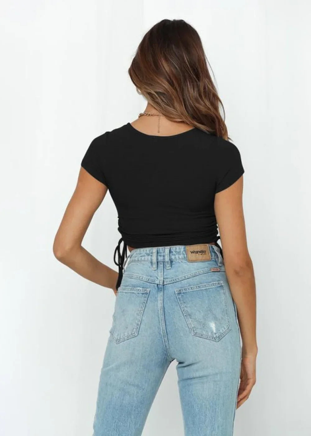 Black ribbed crop top with drawstring sides and light wash high-waisted jeans.
