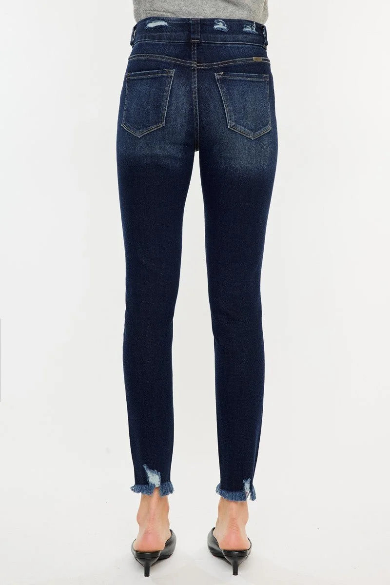 Back view of dark wash distressed denim jeans with frayed hems on model.