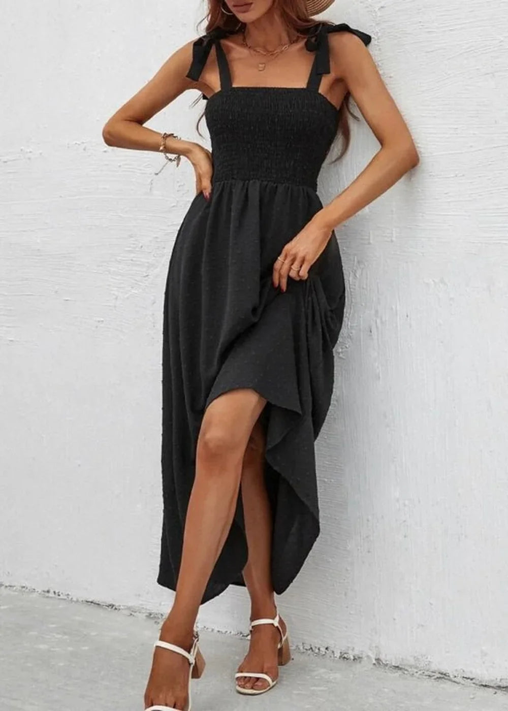 Black smocked sundress with tie straps and a flowing midi skirt, shown on a model.