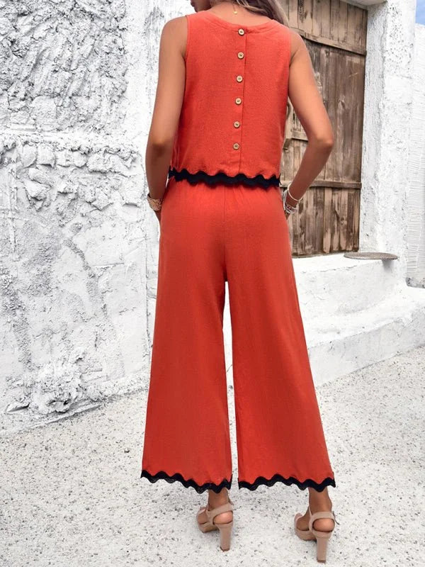Orange wide-leg jumpsuit with black scalloped trim and button-back top, worn by a model.