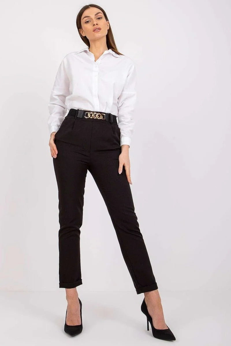 Full-length shot of a woman wearing black high-waisted trousers with a cinched waist and a gold chain belt, paired with a ...