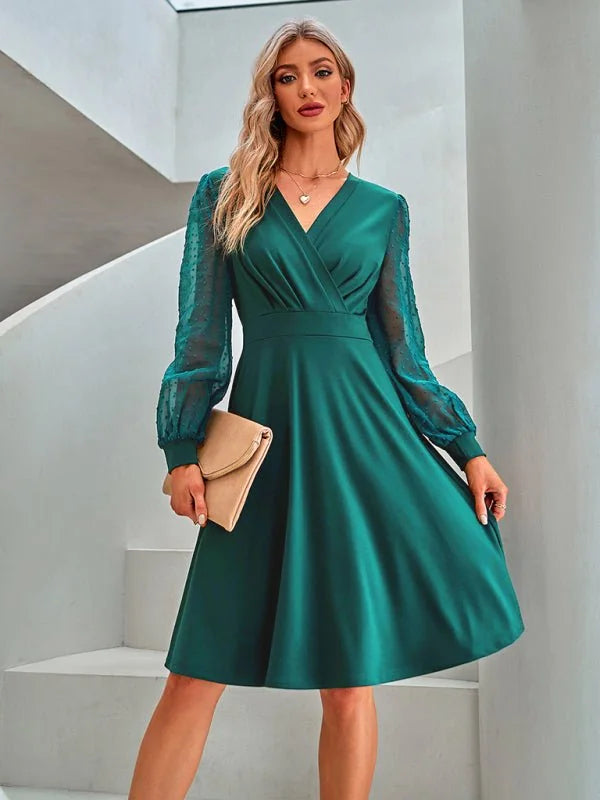 Emerald green faux-wrap dress with sheer polka dot sleeves and a V-neck, held by a model with a tan clutch.