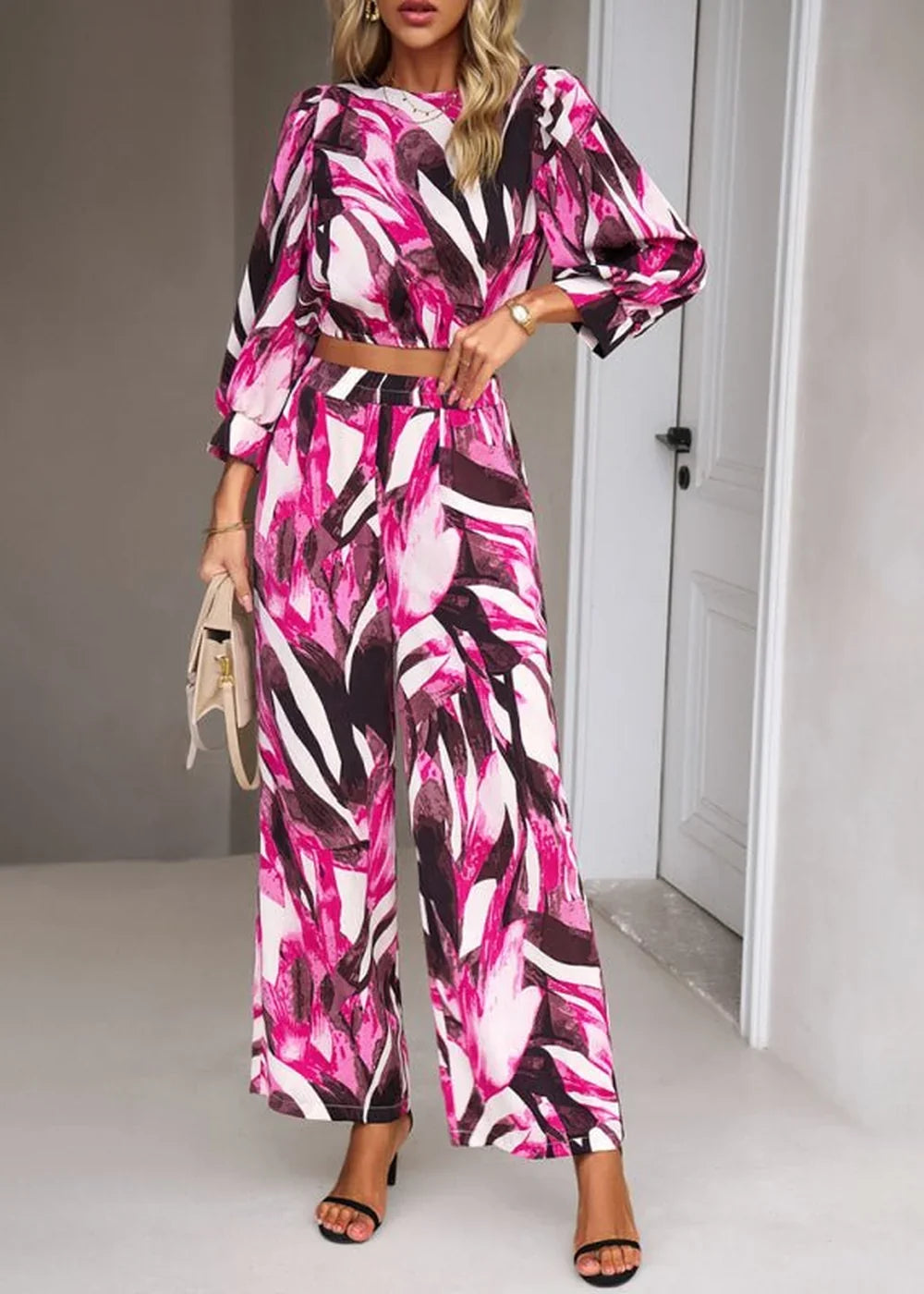 Full-length view of a woman in a pink, white, and black abstract print cropped top and wide-leg pants.