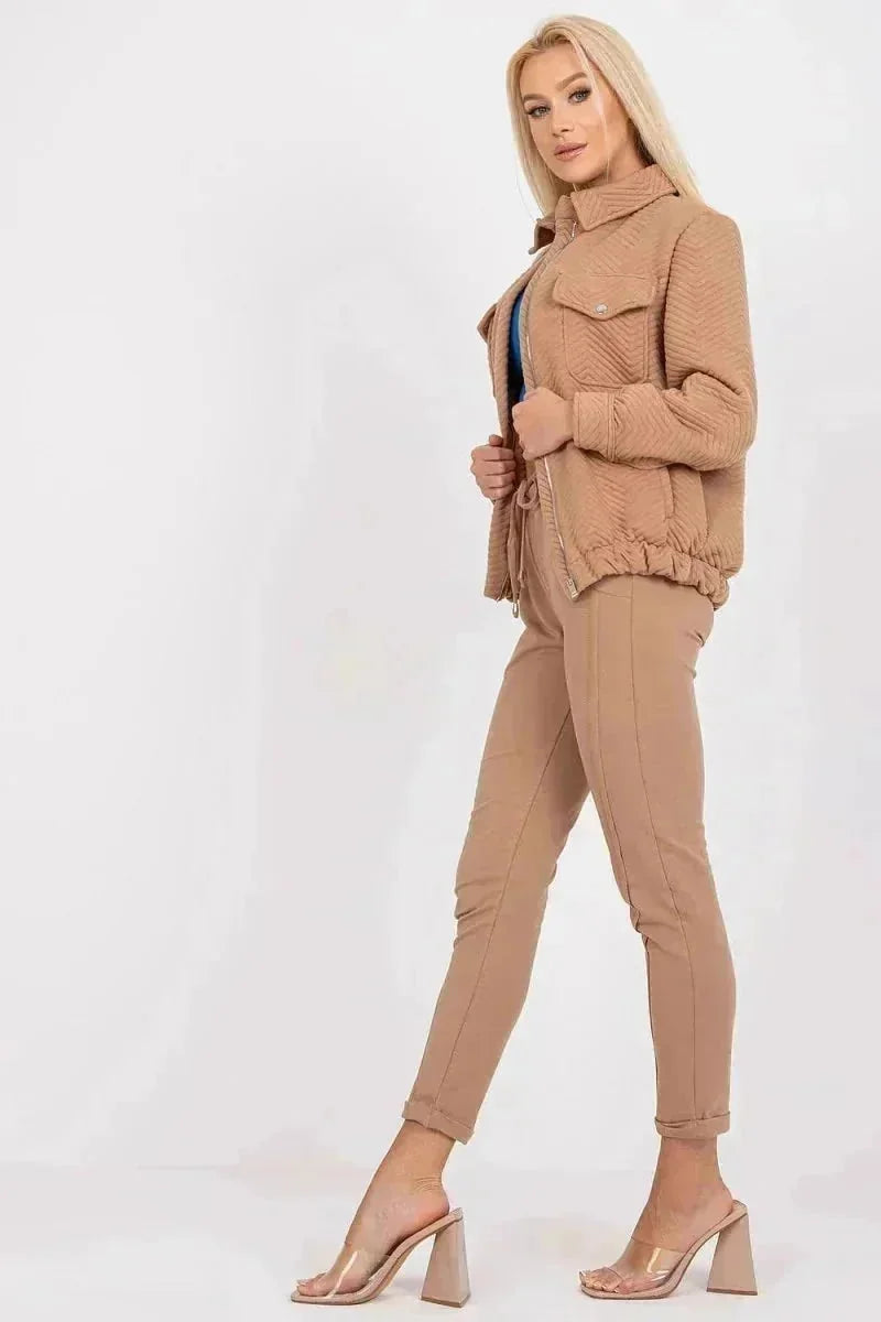 Tan quilted bomber jacket with zip-front and drawstring waist, worn by a model with matching pants and clear heels.