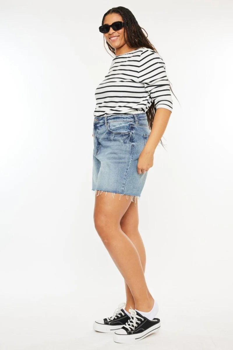 Light wash denim shorts with frayed hem, on a model wearing a striped top and black sneakers.