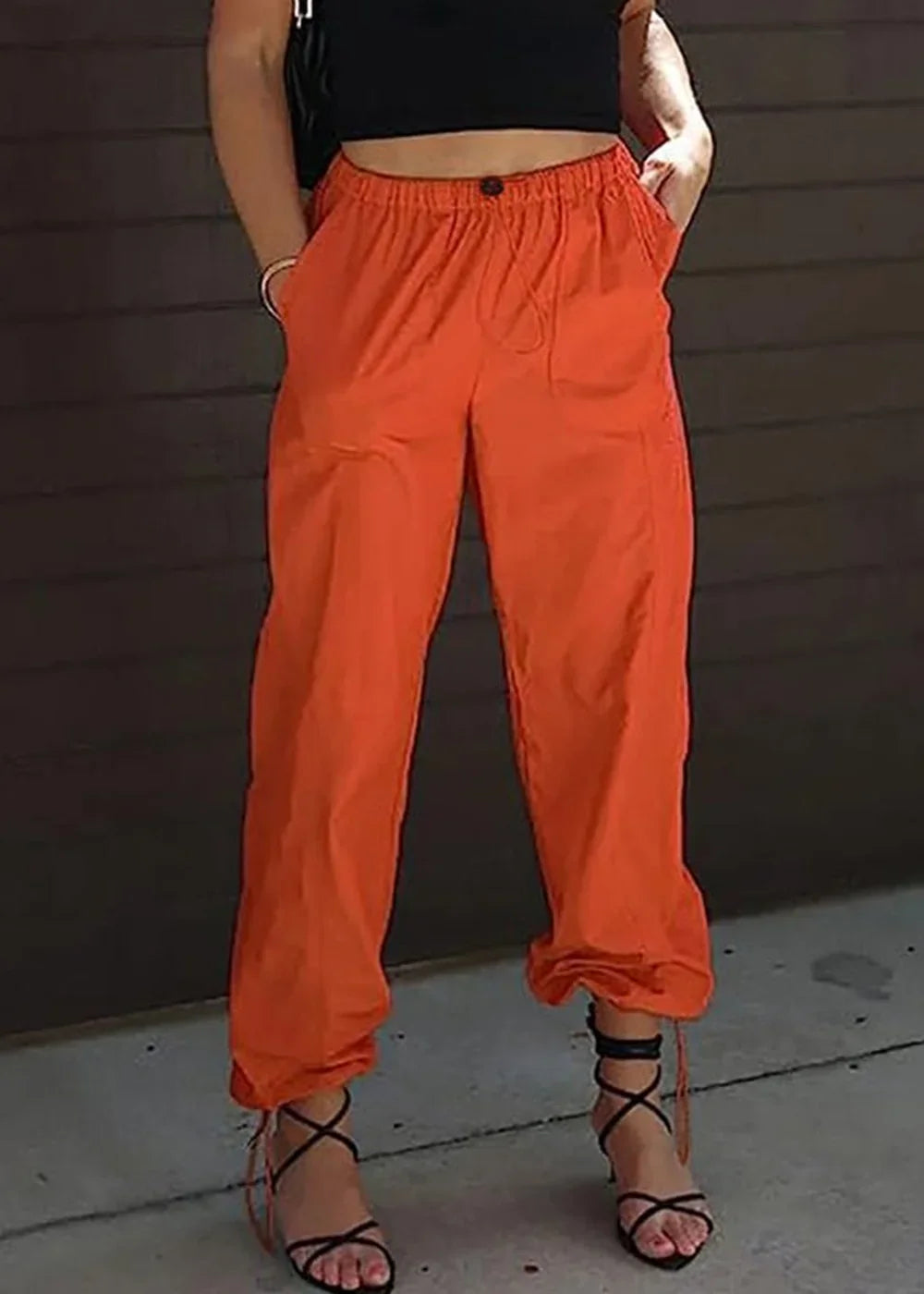 Orange polyester jogger pants with drawstring waist and lace-up ankles on model.