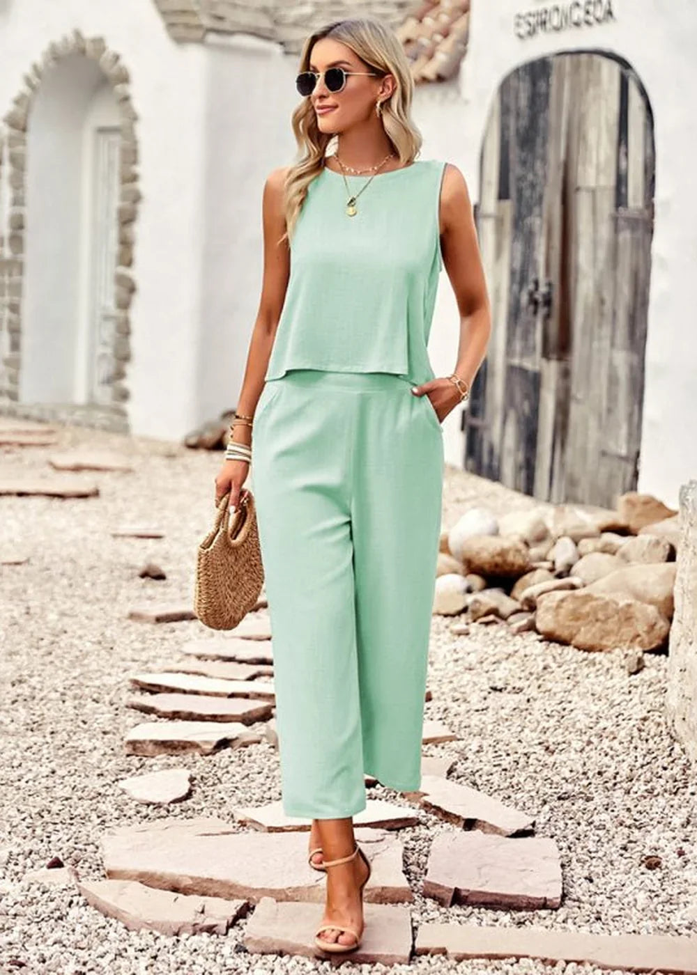 Light mint green sleeveless wide-leg jumpsuit with a cropped top, on a woman with sunglasses and a straw bag.