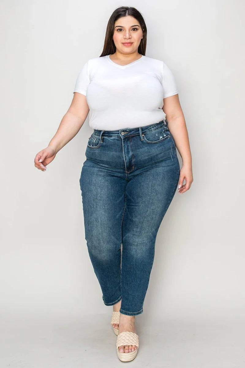 Full-length shot of a woman wearing high-waisted, medium-wash denim jeans with a white v-neck t-shirt.