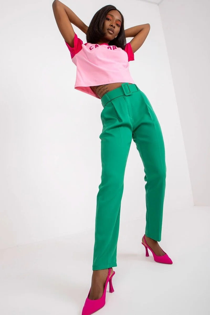 Emerald green high-waisted pants with a belt and pink slingback heels on a model.