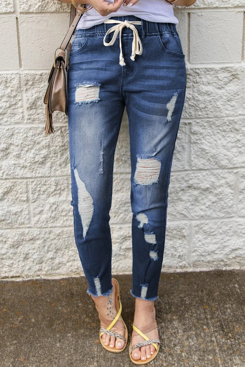 Distressed dark wash denim joggers with a drawstring waist and frayed hem.