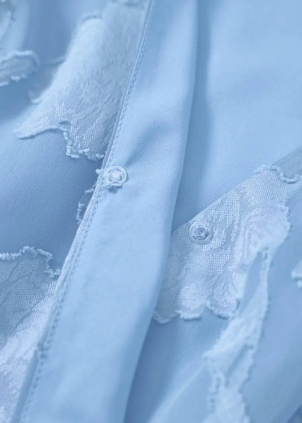Close-up of a light blue polyester dress with delicate white floral lace trim and button details.