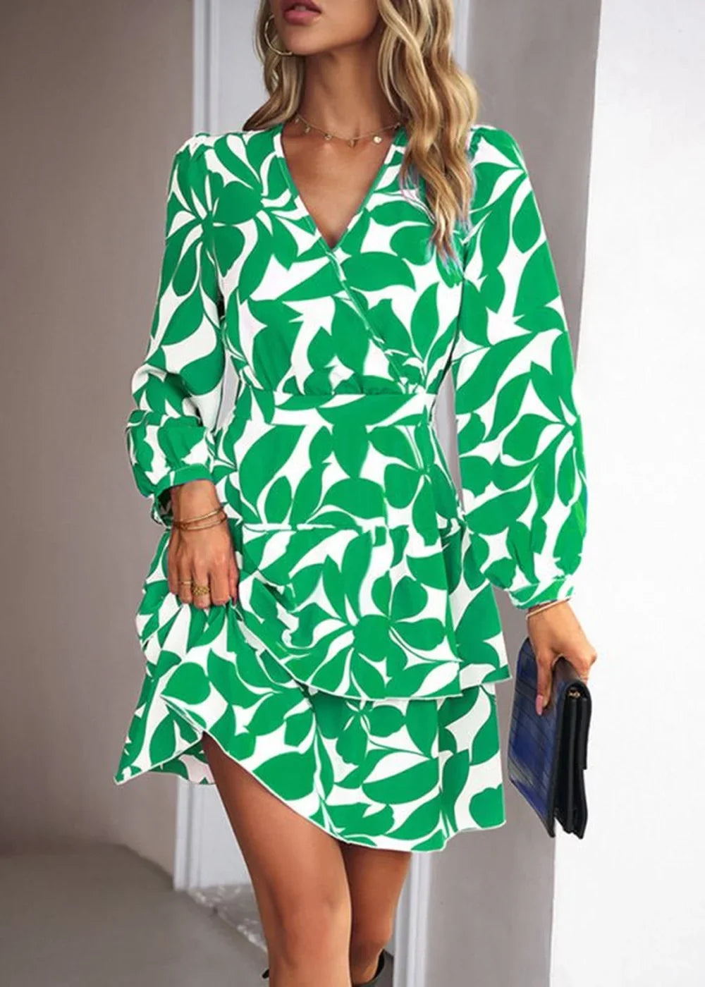 Green and white leaf print wrap dress with ruffled hem and long sleeves, held by a model.