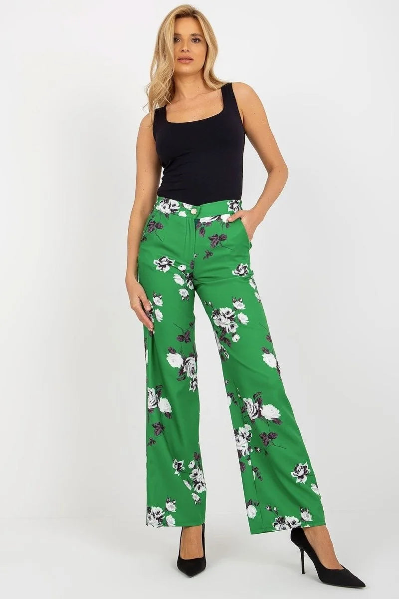 Woman in wide-leg green pants with a white and black floral pattern, paired with a black tank top.