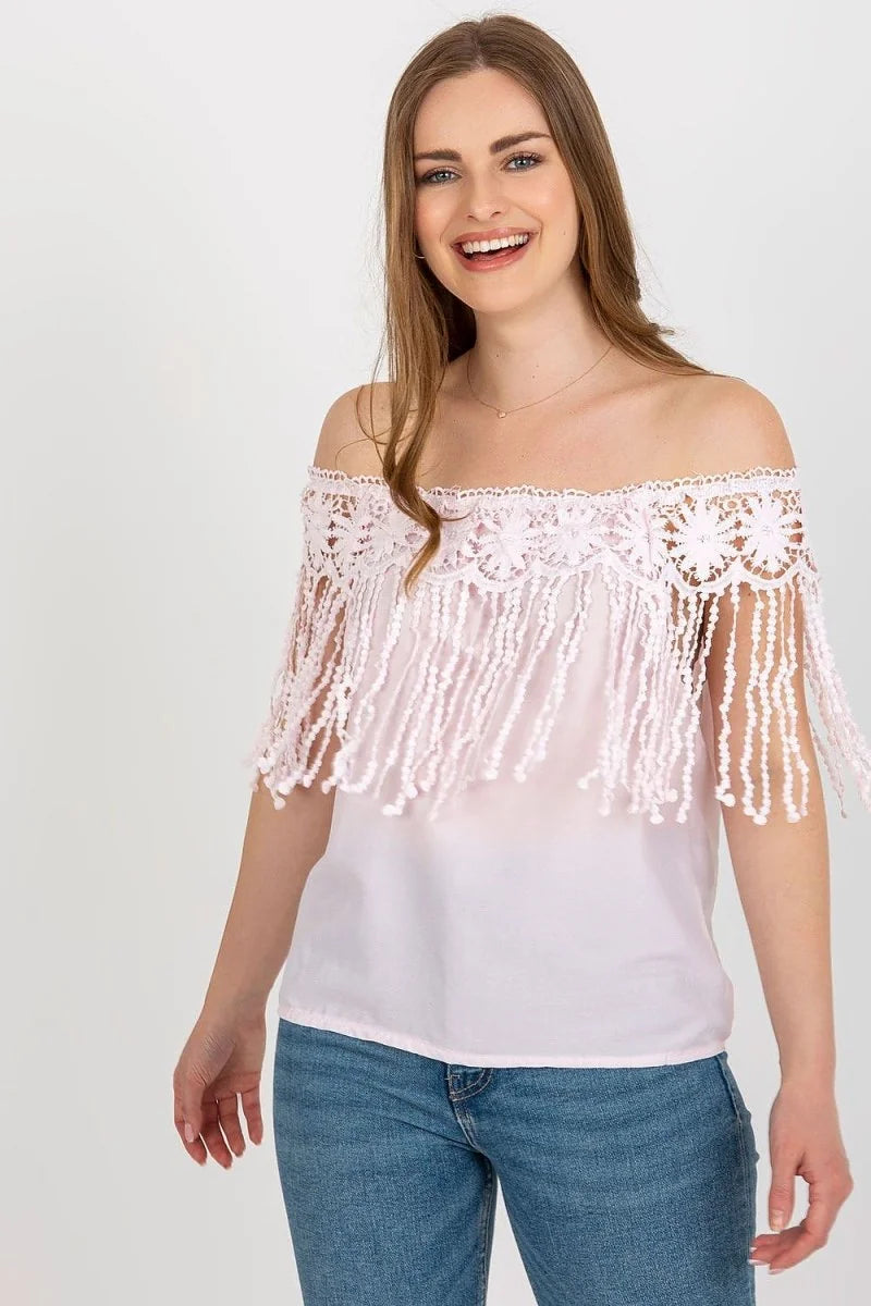 Light pink off-the-shoulder top with intricate lace overlay and fringe detail, paired with blue denim jeans.