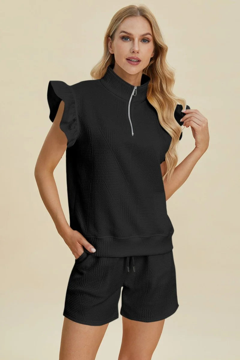 Black quilted short suit with ruffled sleeves and a quarter-zip neckline on a model.